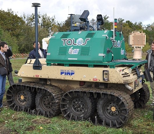 A six-wheeled all-terrain platform on grassland, carrying a sensor head and antennas on a short mast.