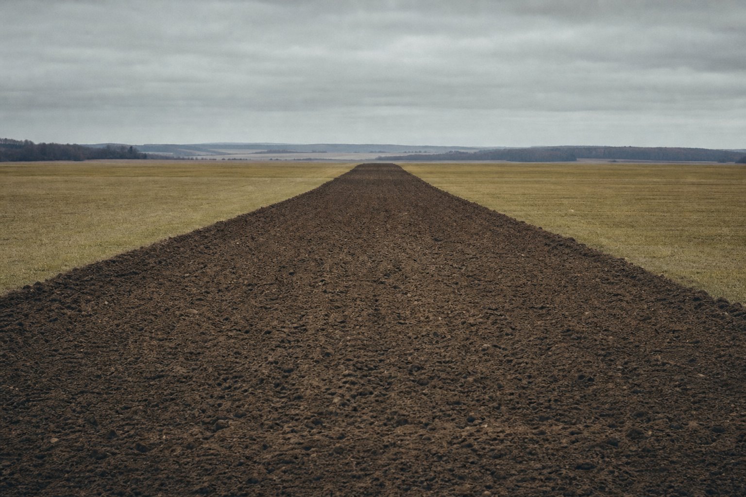 A wide strip of freshly ploughed bare earth running straight across flat farmland.