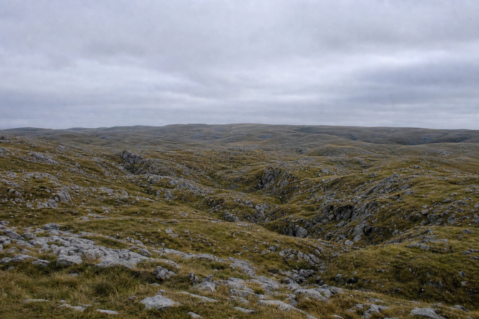 Bare upland of broken rock and short grass with folds and gullies running away from the viewer.